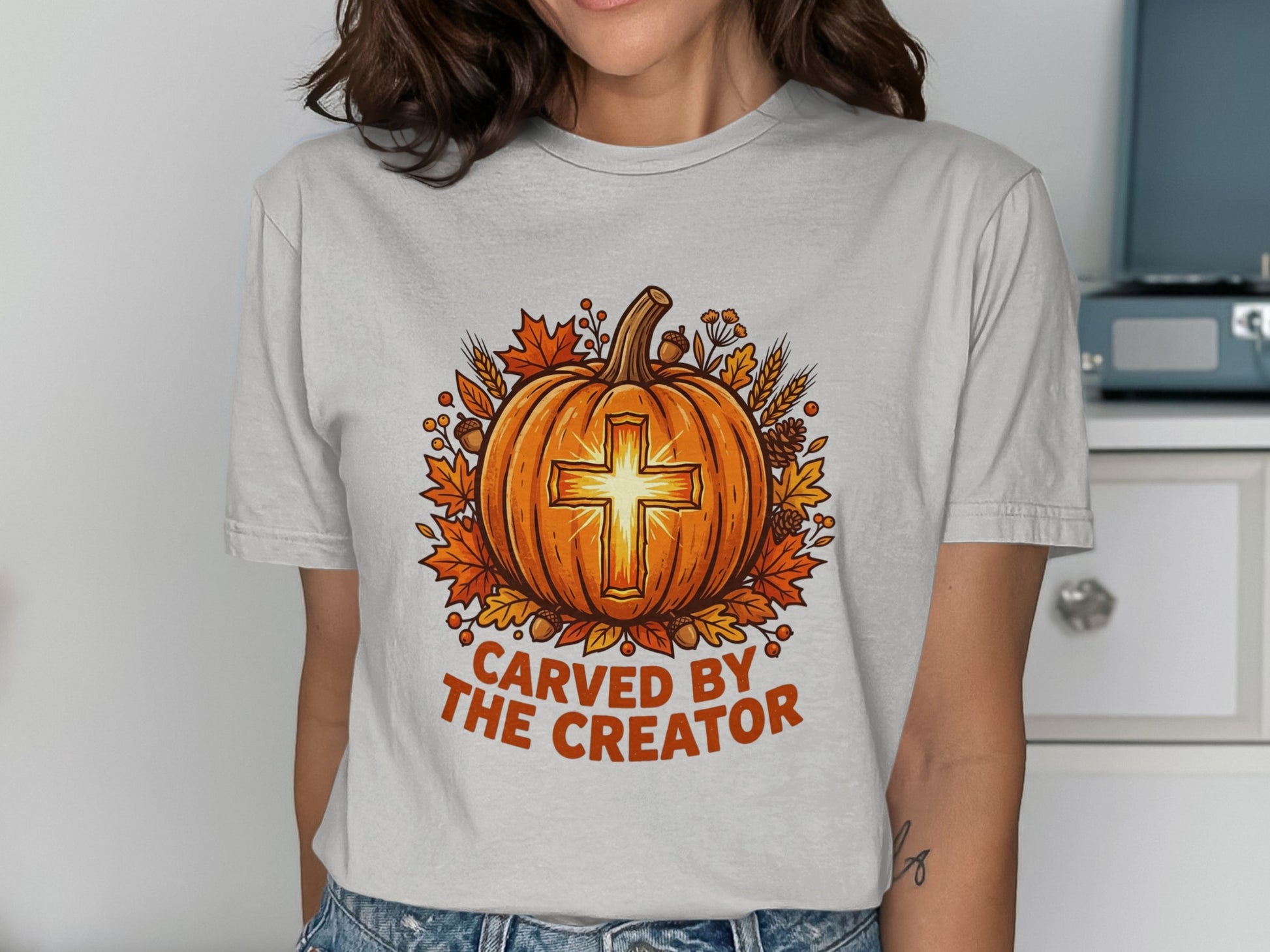 Pumpkin with cross design, "Carved by the Creator" text, surrounded by autumn leaves.