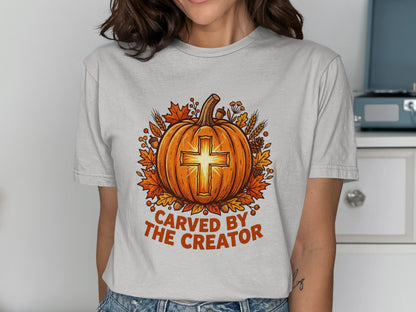 Pumpkin with cross design, "Carved by the Creator" text, surrounded by autumn leaves.
