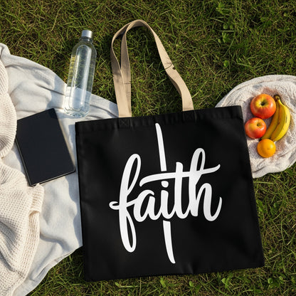 Black tote bag with white "faith" text on a picnic blanket with fruit and water.