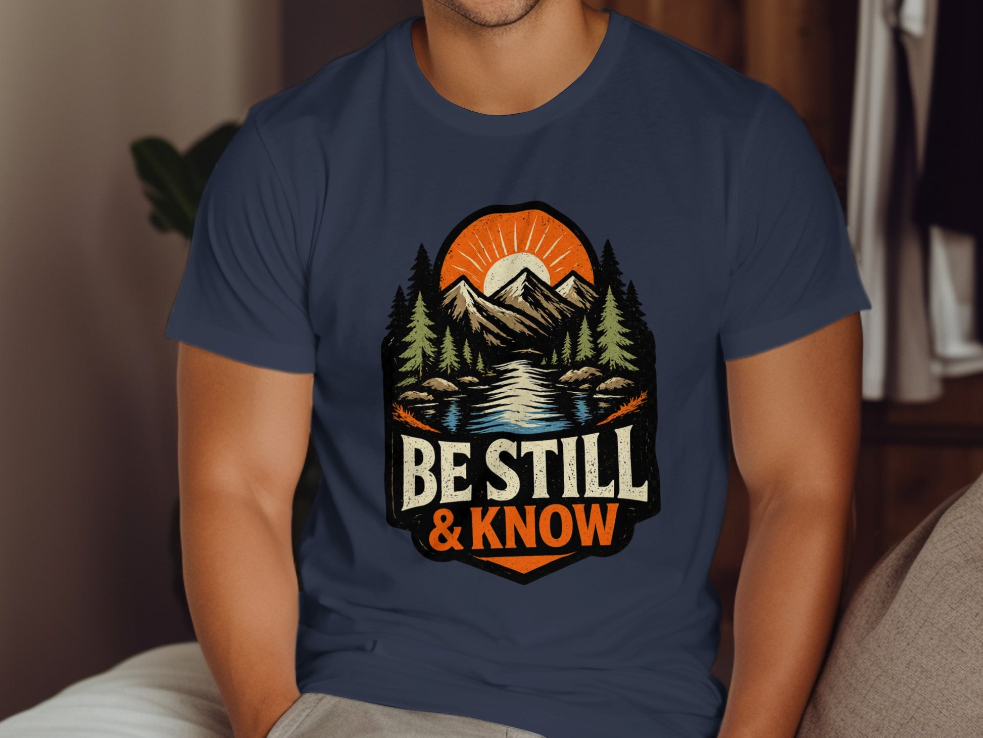 Navy t-shirt with mountains, sun, and "Be Still & Know" text.