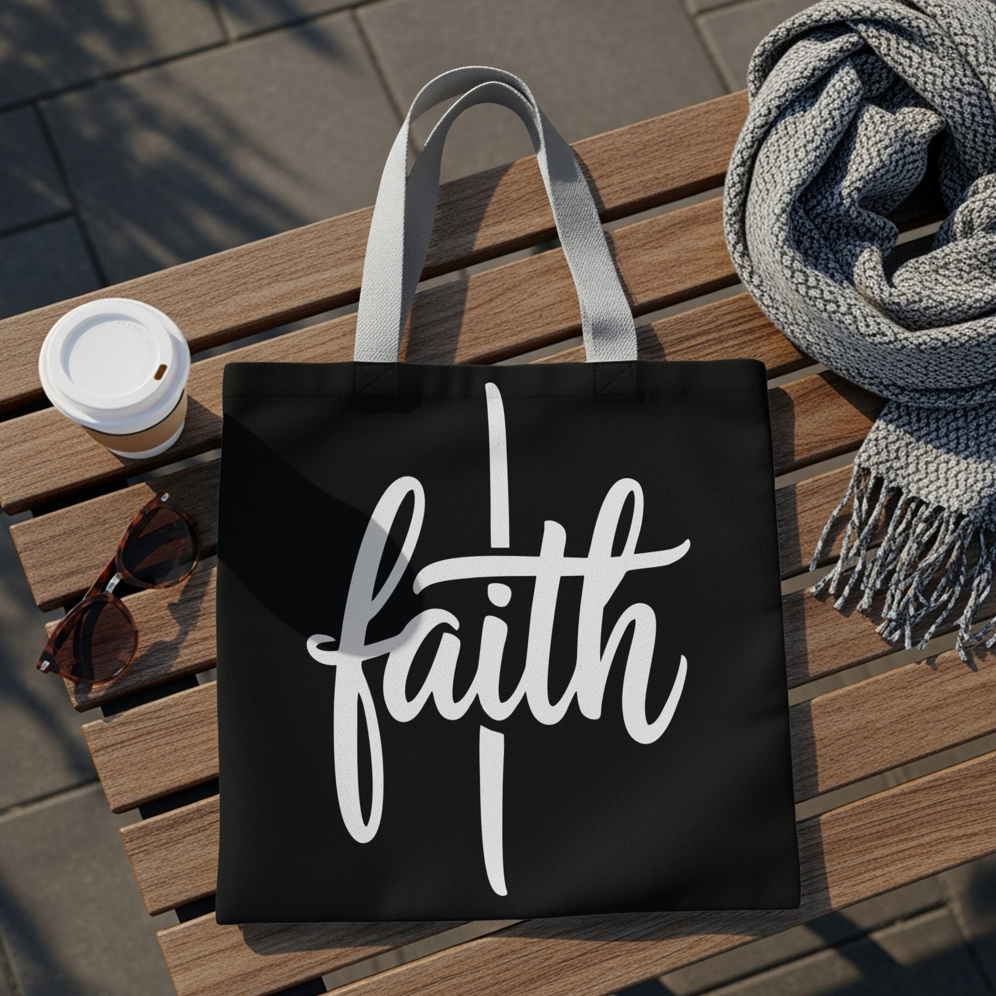 Black tote bag with white "faith" lettering, sunglasses, coffee cup, and scarf.