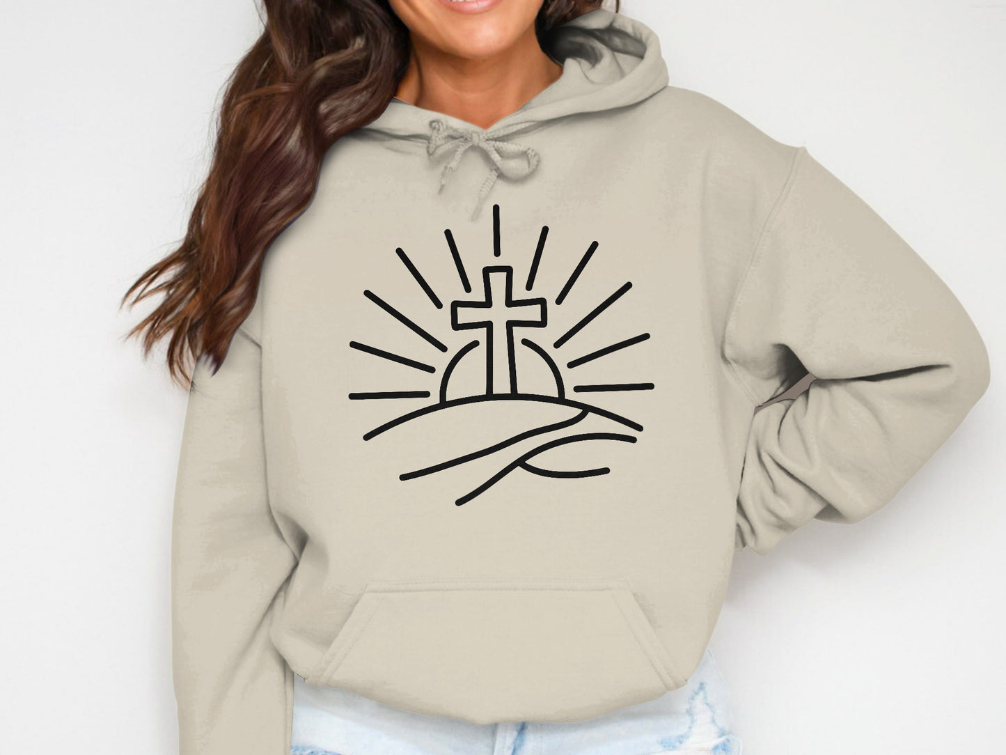 Beige hoodie with a line drawing of a cross rising above hills with sun rays.