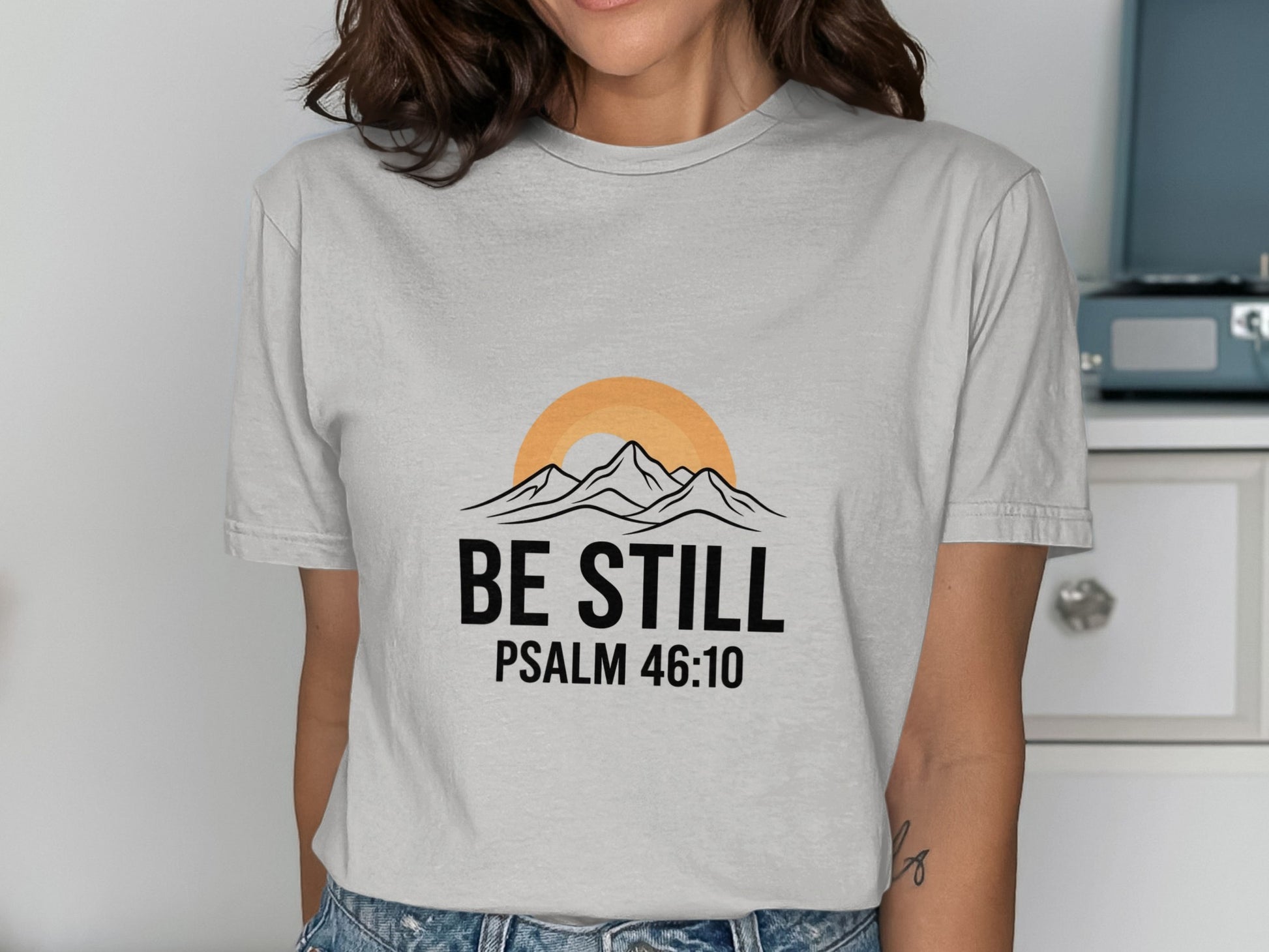 Gray t-shirt with "BE STILL PSALM 46:10" text and mountain sunset graphic.
