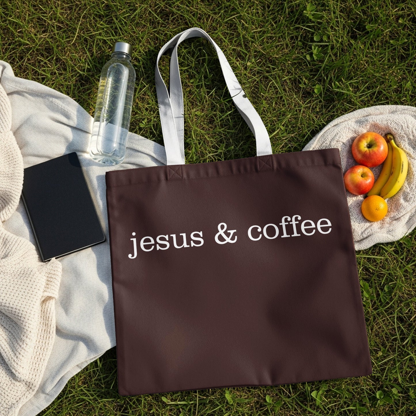 Brown tote bag with white text "jesus & coffee" on grass.