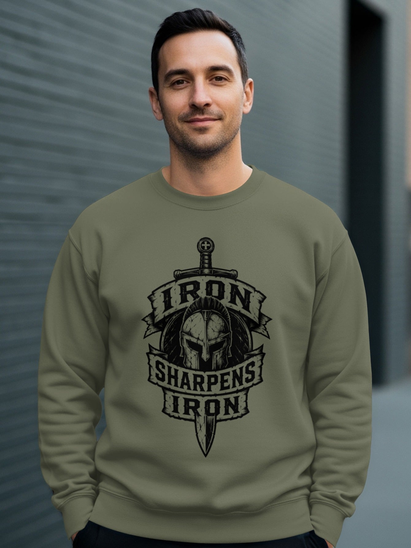 Man wearing olive sweatshirt with "Iron Sharpens Iron" Spartan helmet and sword design.