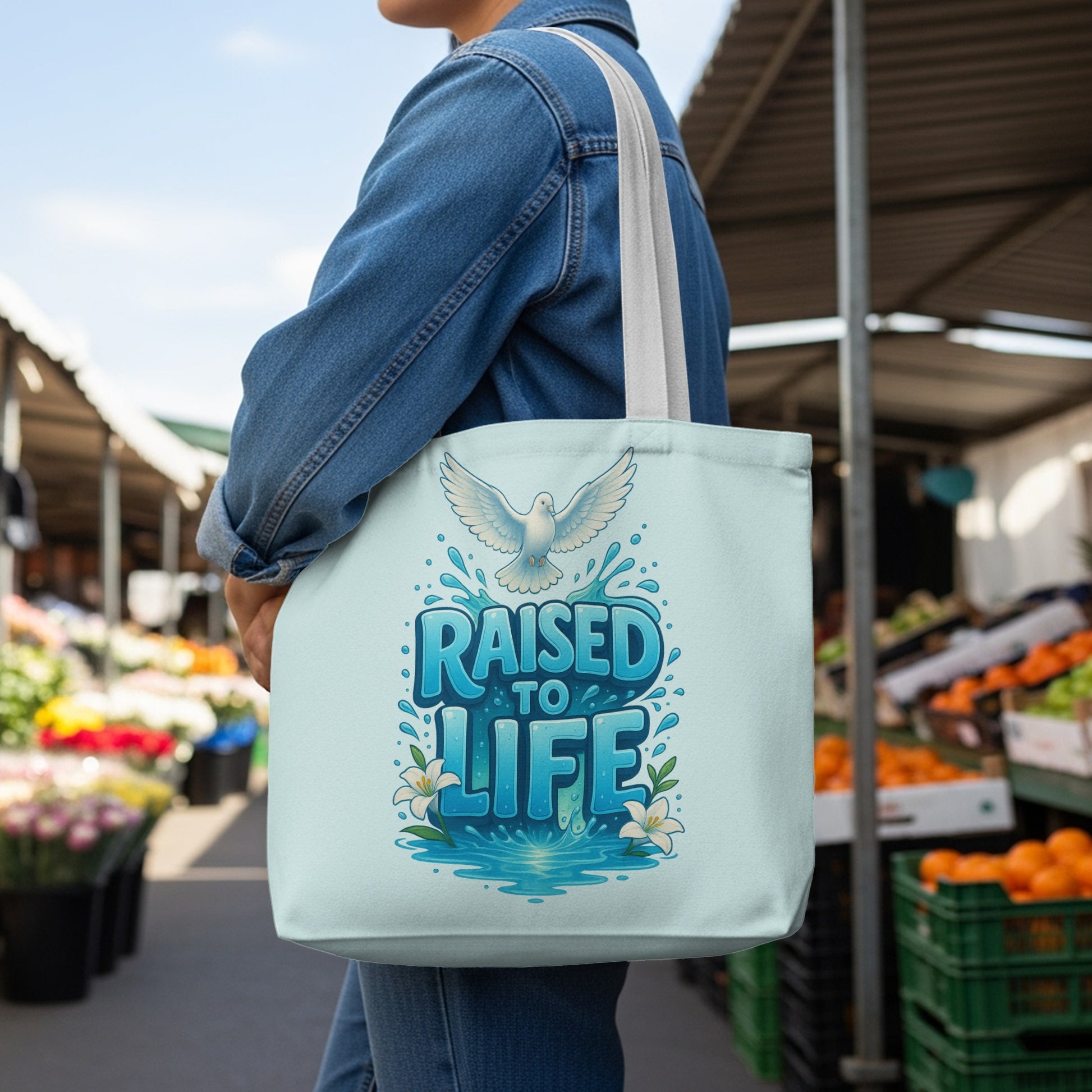 Light blue tote bag with a dove and "RAISED TO LIFE" text in blue lettering.
