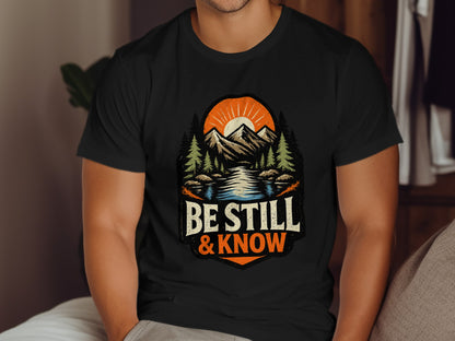 Black t-shirt with "Be Still & Know" text, mountains, and sun graphic.