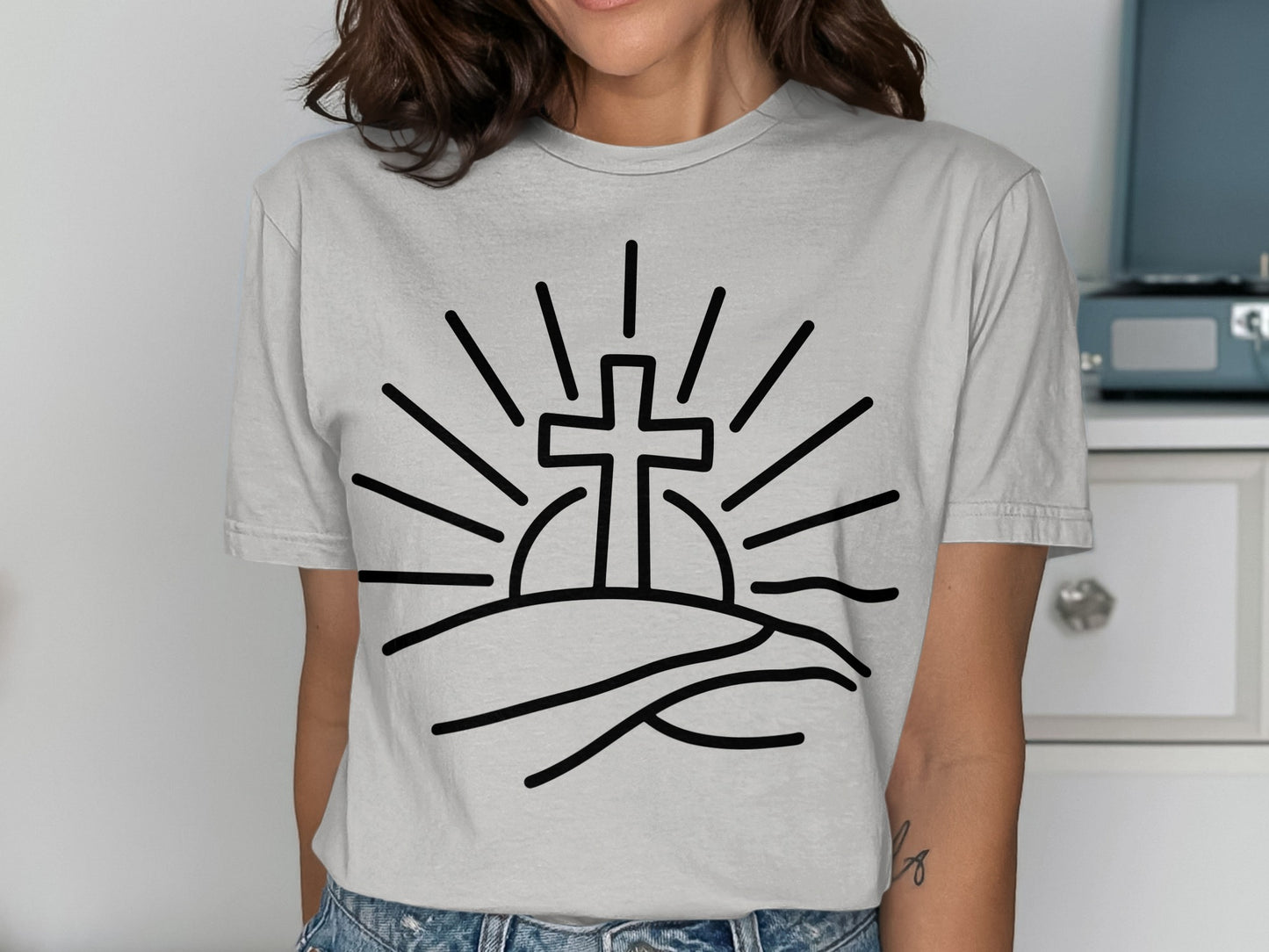 Line art cross with sunburst over rolling hills on a gray t-shirt.