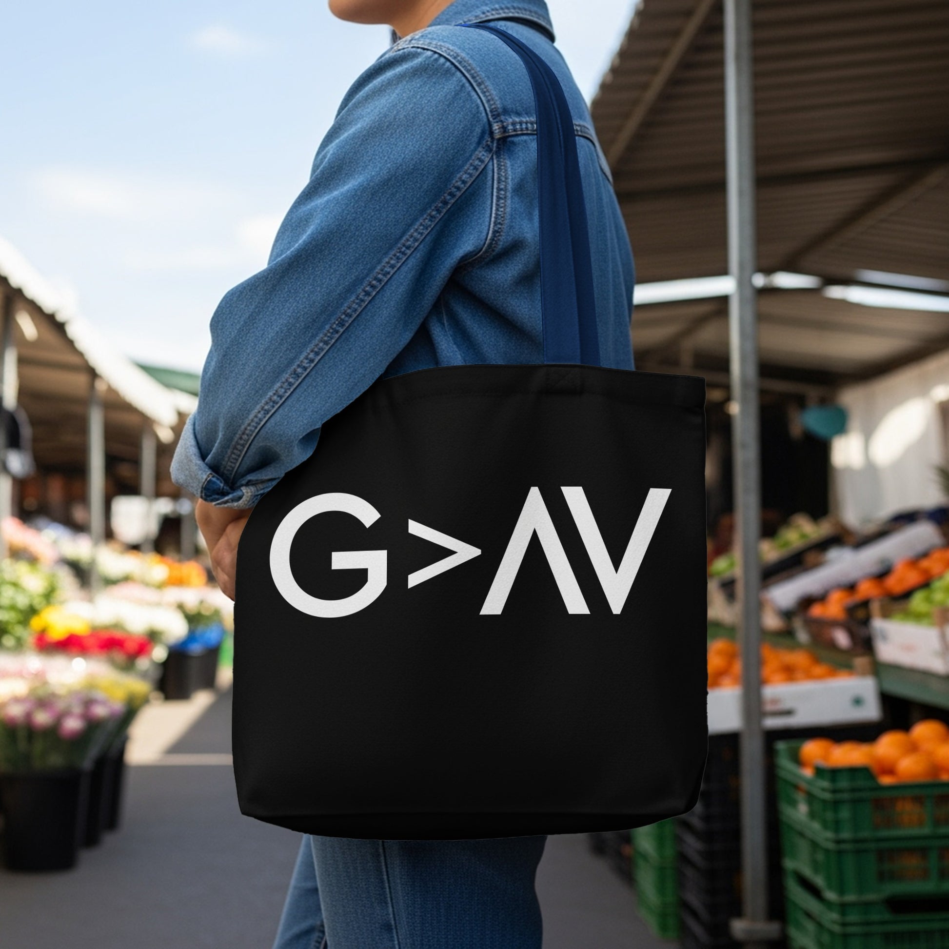 Black tote bag with white "G > AV" text, worn by person in denim jacket.