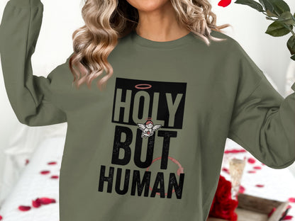 Olive green crewneck sweatshirt with "HOLY BUT HUMAN" text and an angel graphic.
