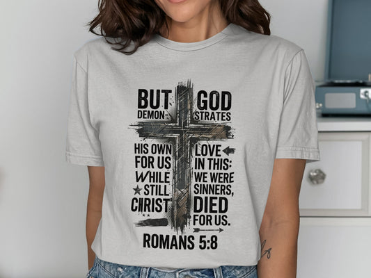 Christian t-shirt with a cross graphic and scripture from Romans 5:8.
