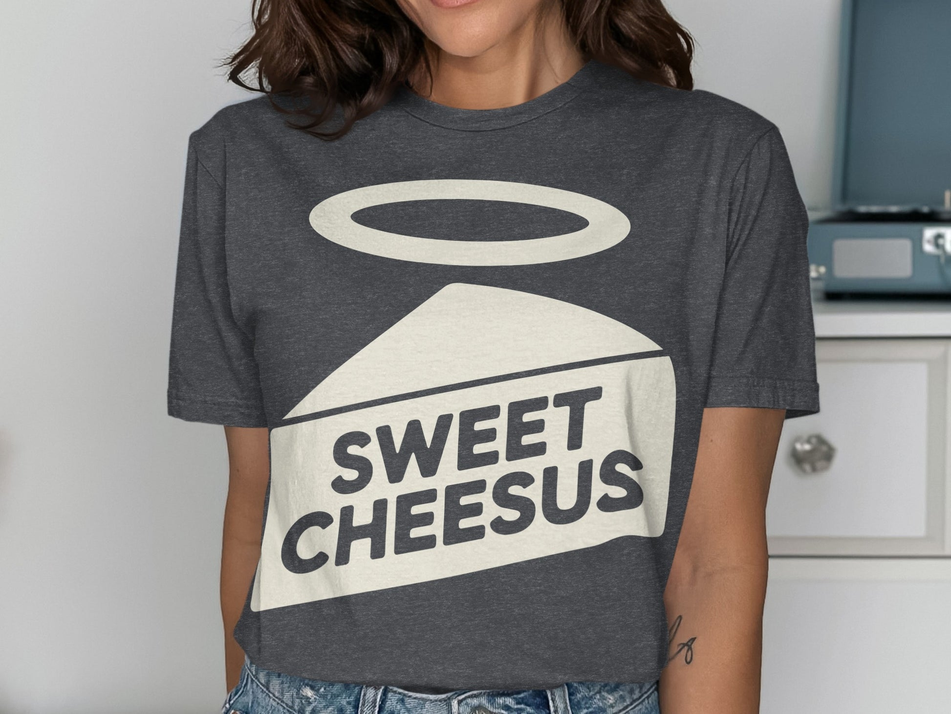 Dark t-shirt featuring a wedge of cheese with a halo and "SWEET CHEESUS" text.
