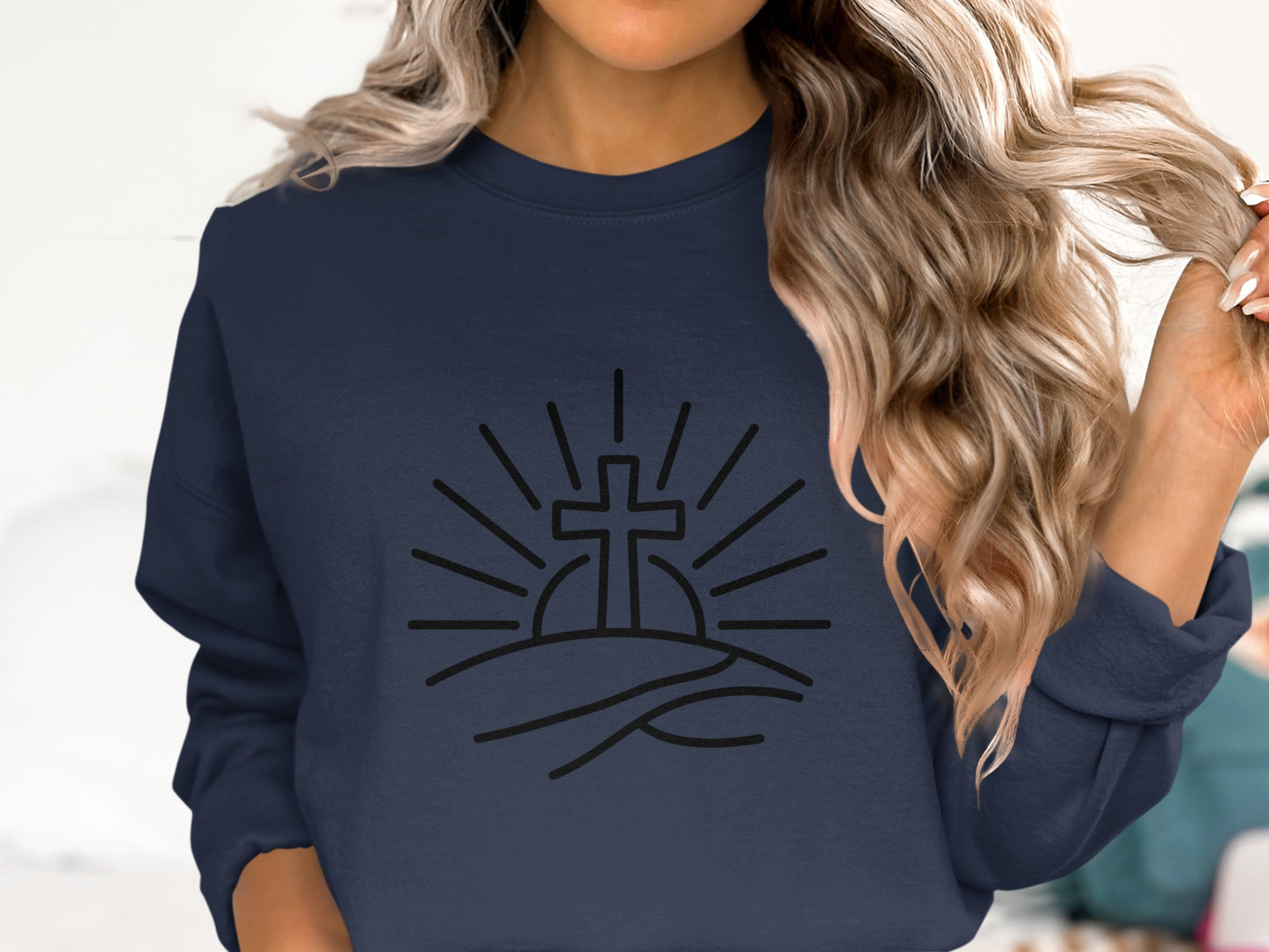 Navy sweatshirt with sun rays and cross graphic on a hill.