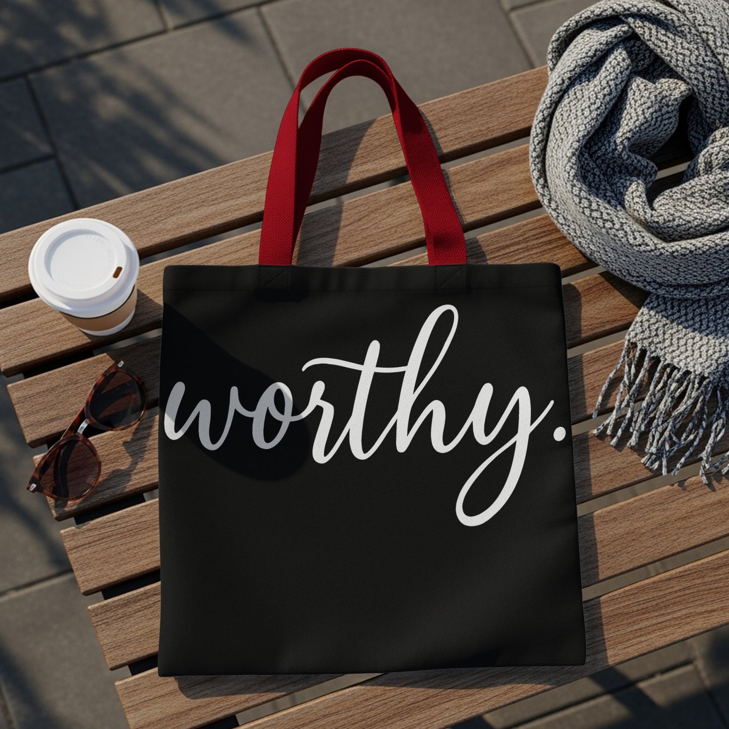 Black tote bag with red straps and "worthy." in white script text.