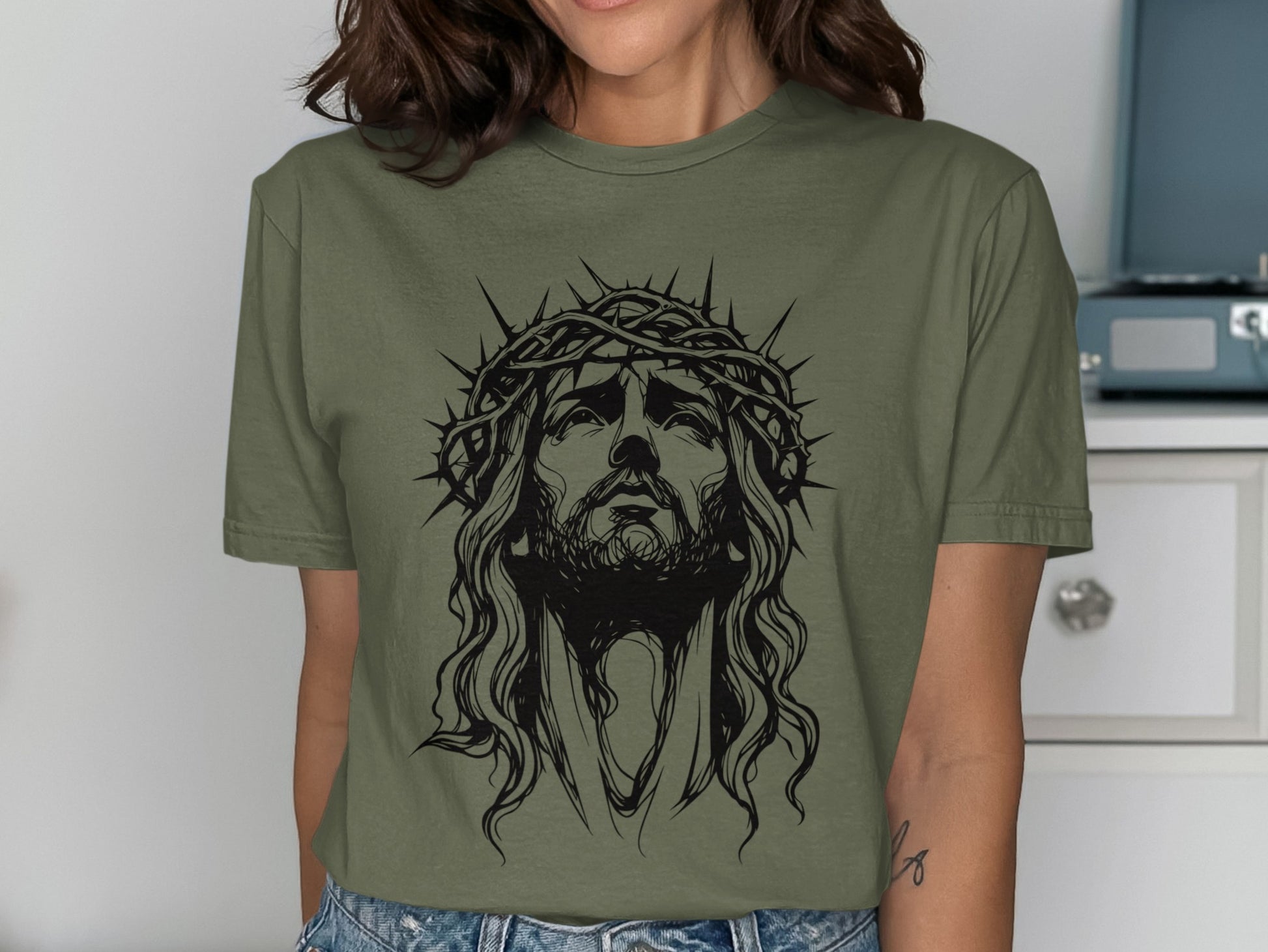Line art of Jesus with a crown of thorns on a green t-shirt.