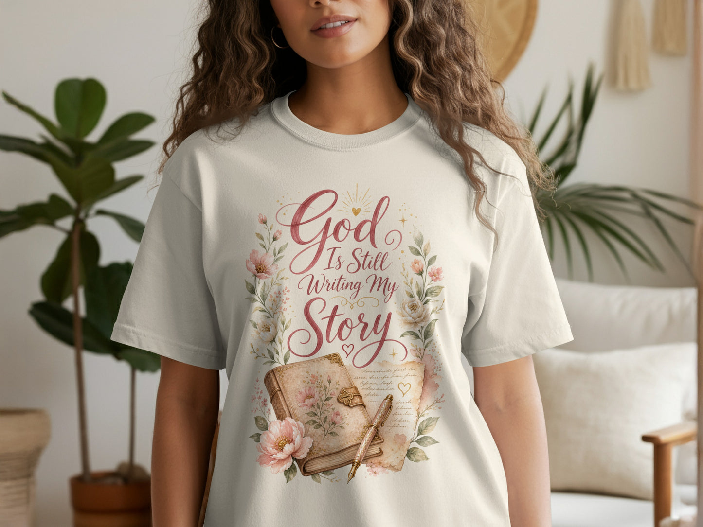T-shirt with "God Is Still Writing My Story" text, book, and flowers.