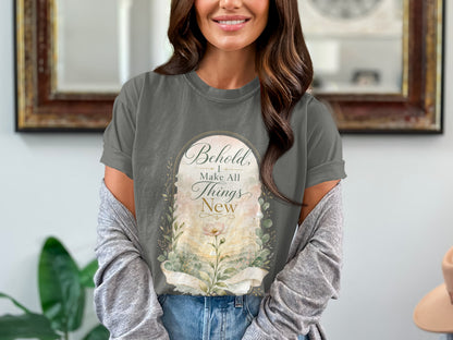 Graphic t-shirt with text "Behold, I Make All Things New" and floral design.