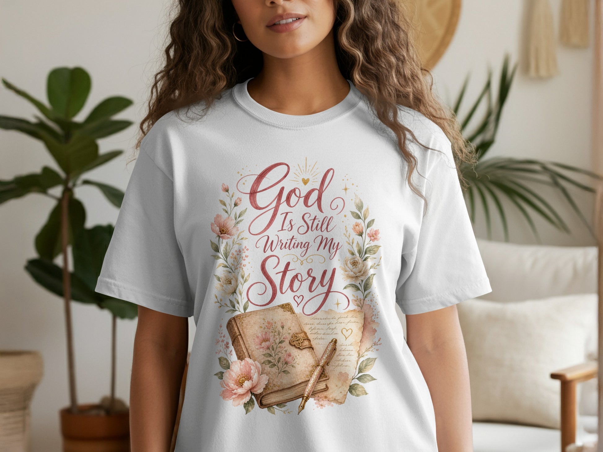 White t-shirt with "God Is Still Writing My Story" text, floral wreath, and open book.