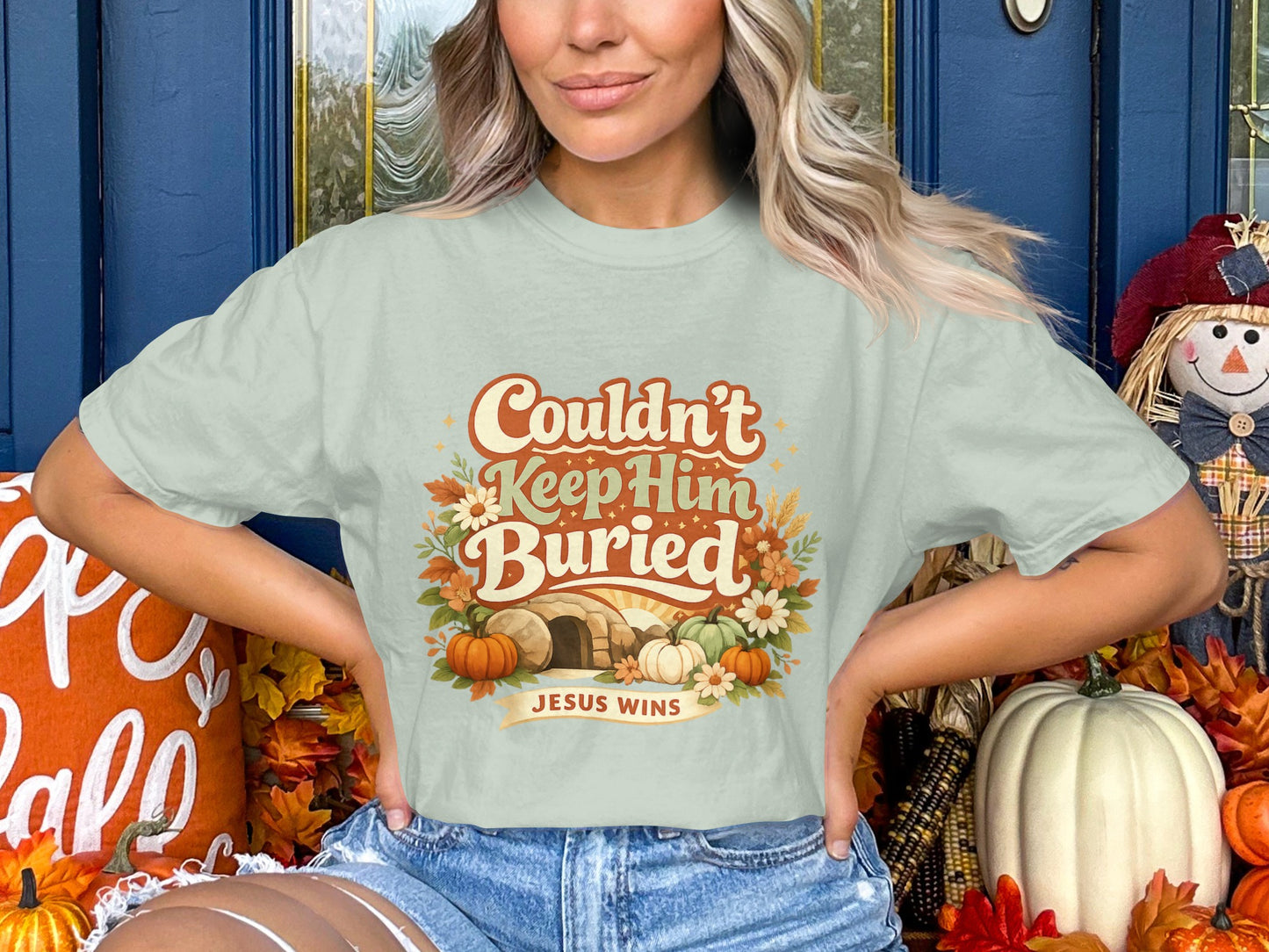 Light green t-shirt with "Couldn't Keep Him Buried Jesus Wins" text, tomb, and pumpkins.