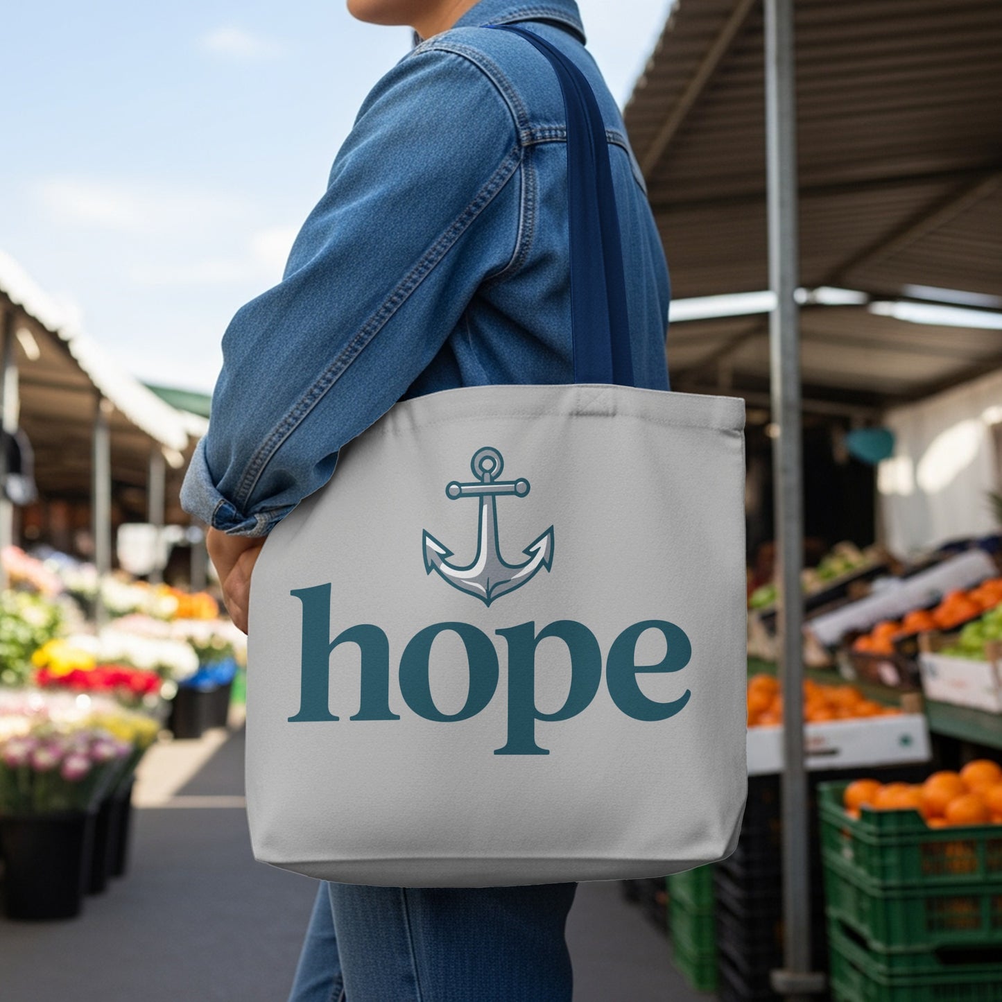 Grey tote bag with anchor and "hope" text, worn by a person in denim.