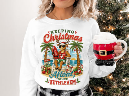 Reindeer lifeguard on beach, wearing sunglasses, holding mug, text reads "Keeping Christmas Since Bethlehem".