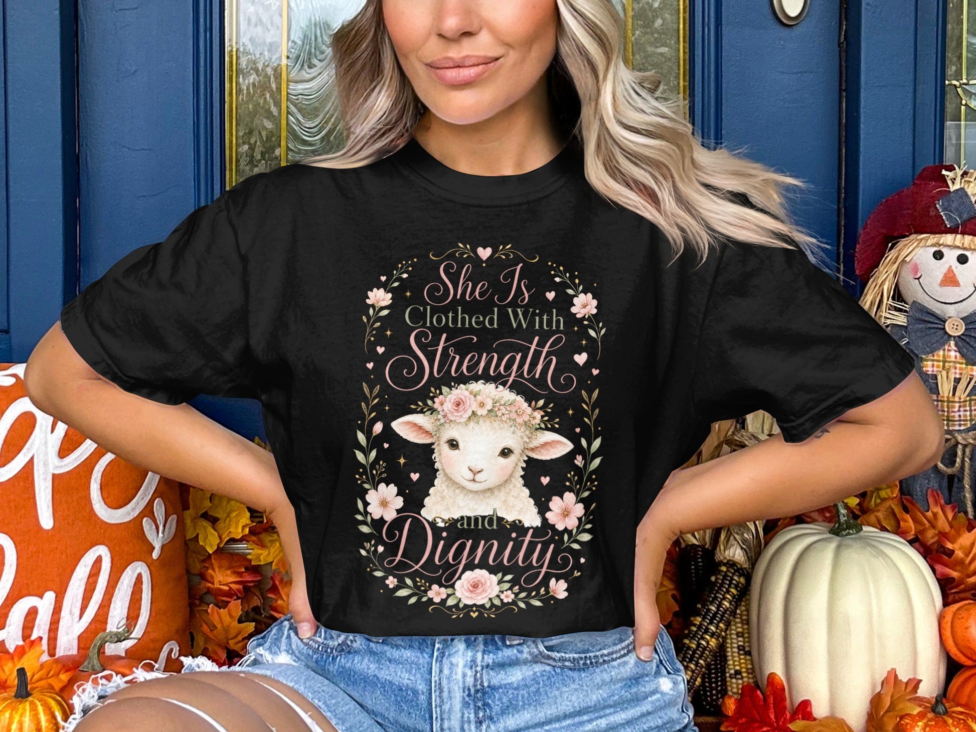Black t-shirt with a floral wreath framing a lamb and text: "She Is Clothed With Strength and Dignity."