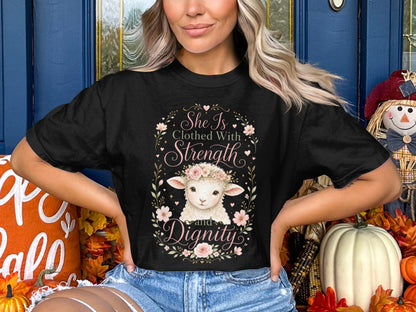 Black t-shirt with a floral wreath framing a lamb and text: "She Is Clothed With Strength and Dignity."
