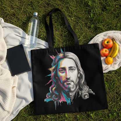 Black tote bag with colorful Jesus portrait on grass with fruit and notebook.