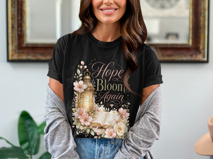 Black t-shirt with "Hope Bloom Again" text, a lantern, open book, and floral design.