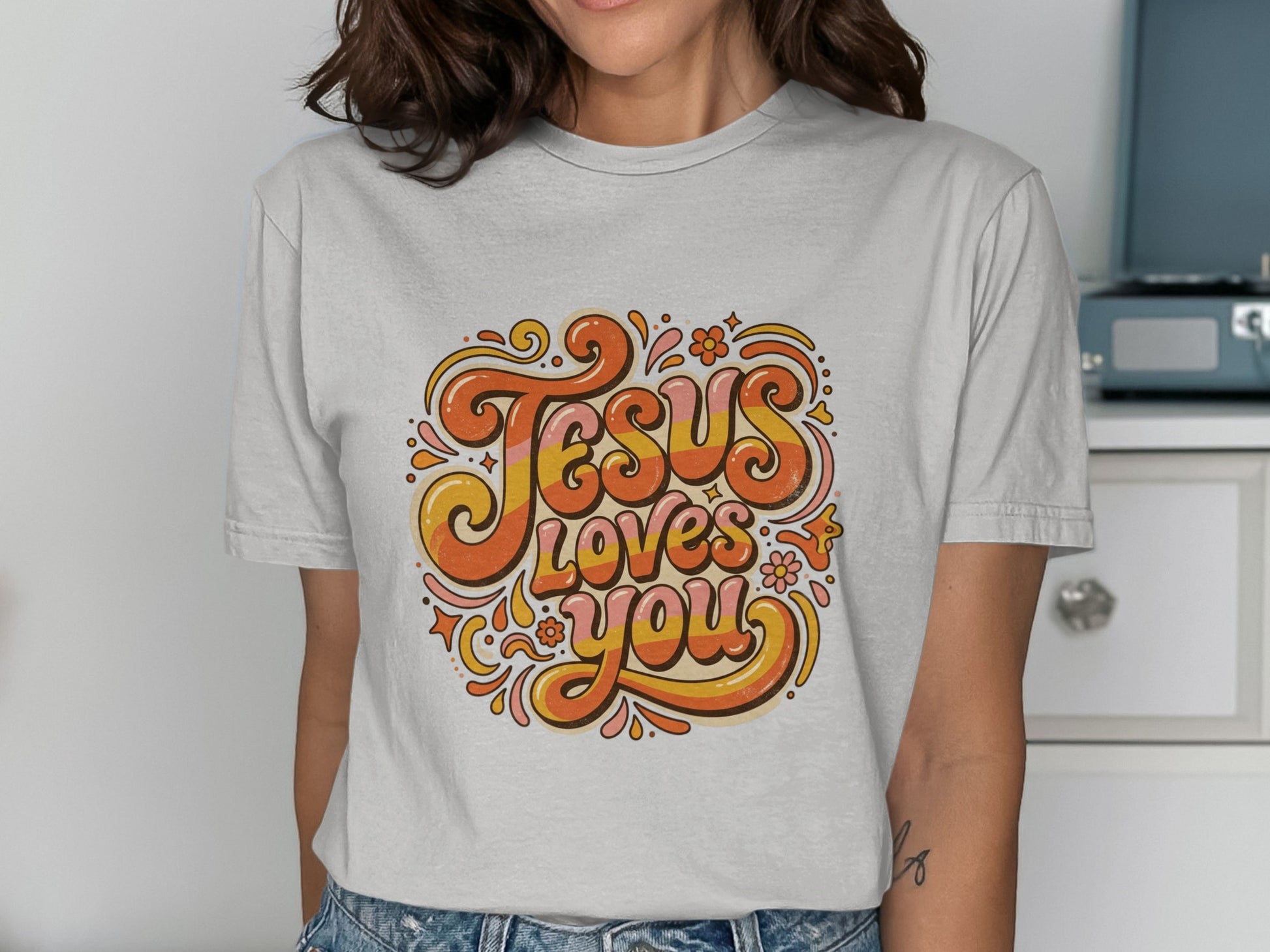 Retro text "Jesus Loves You" with flowers on a light gray t-shirt.