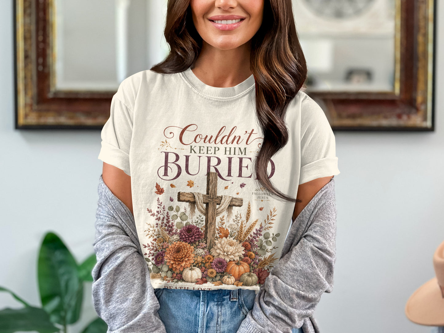 Cream t-shirt with "Couldn't Keep Him Buried" text and floral cross design.
