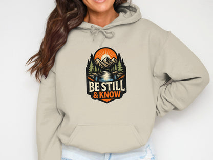Be still & know graphic on a light tan hooded sweatshirt.