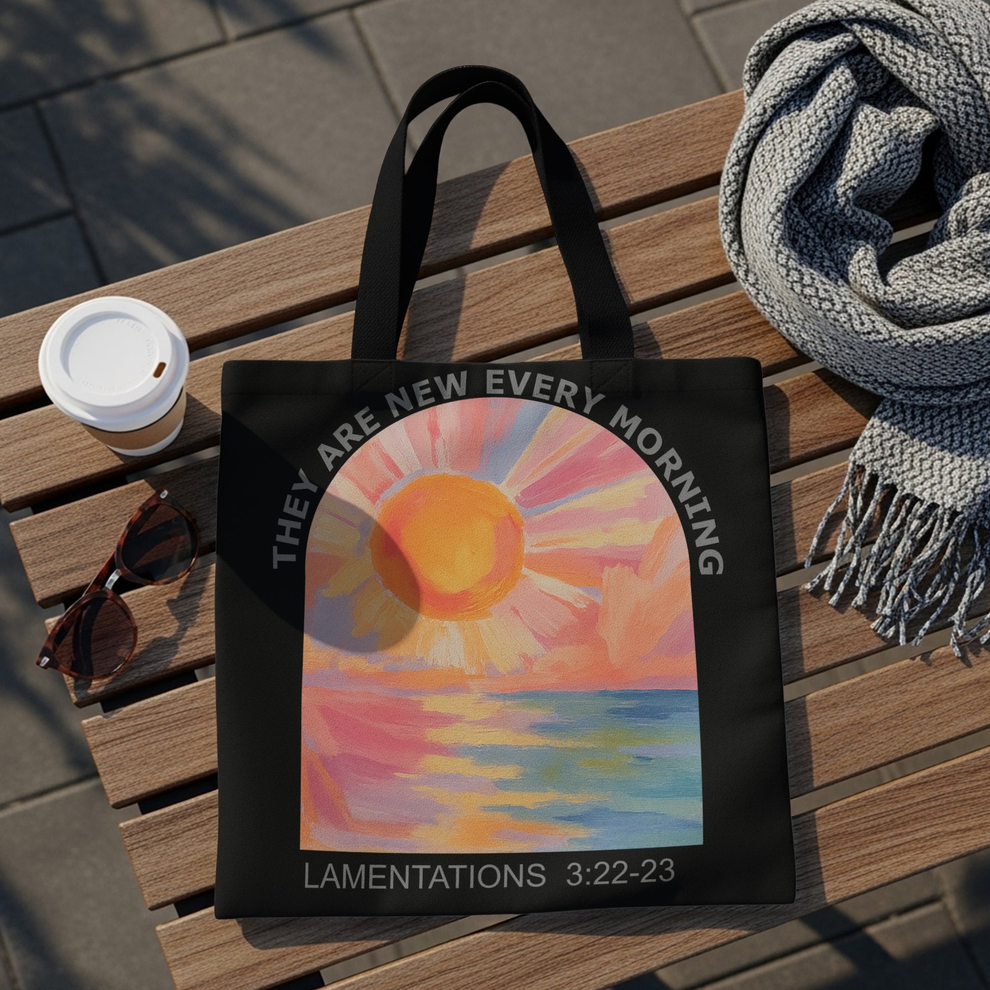 Black tote bag with colorful sunrise over water art and text: "THEY ARE NEW EVERY MORNING LAMENTATIONS 3:22-23".