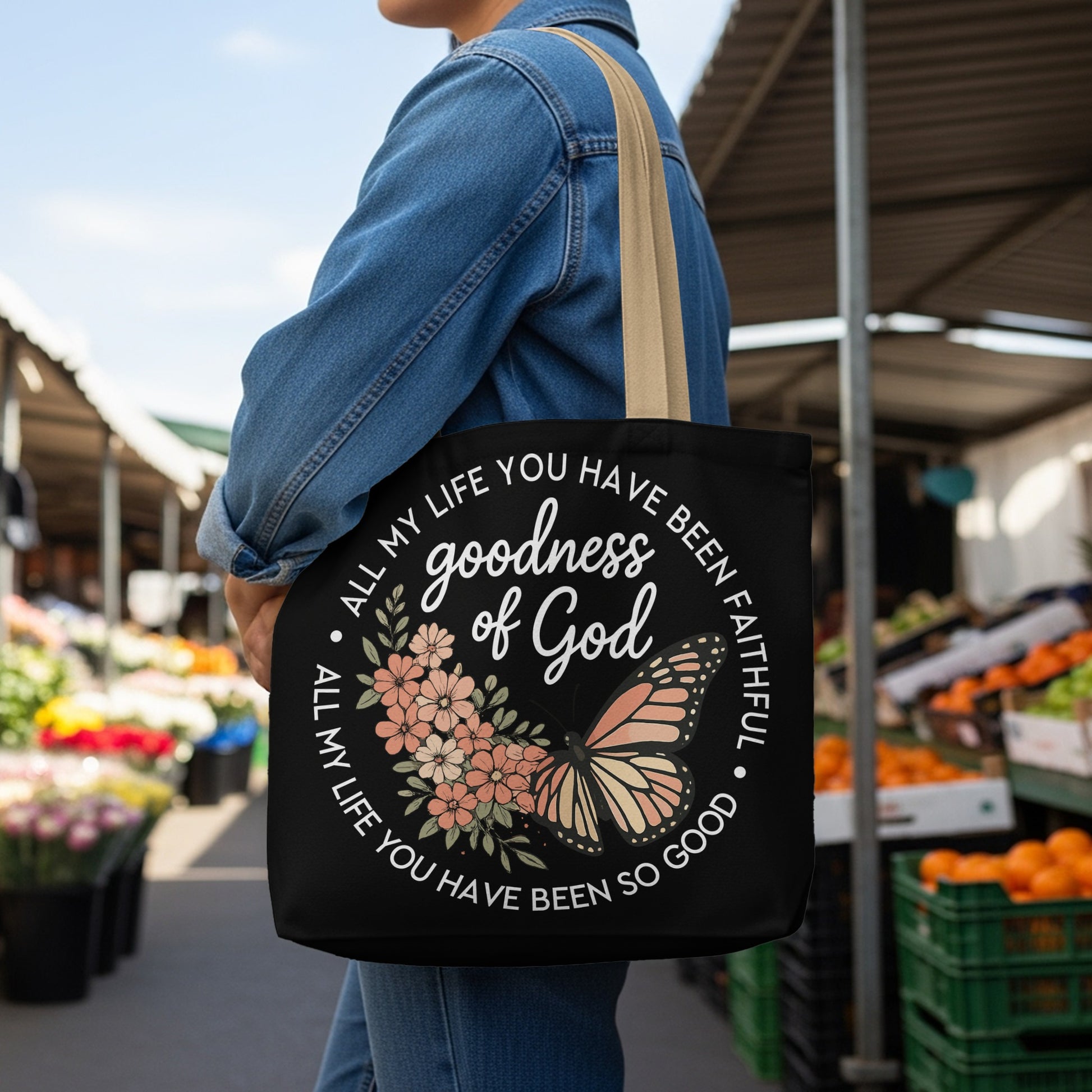 Black tote bag with "goodness of God" text, flowers, and butterfly graphic.