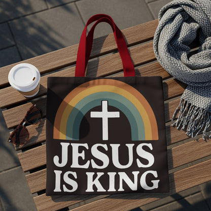 Black tote bag with white text "JESUS IS KING" and a rainbow cross graphic.