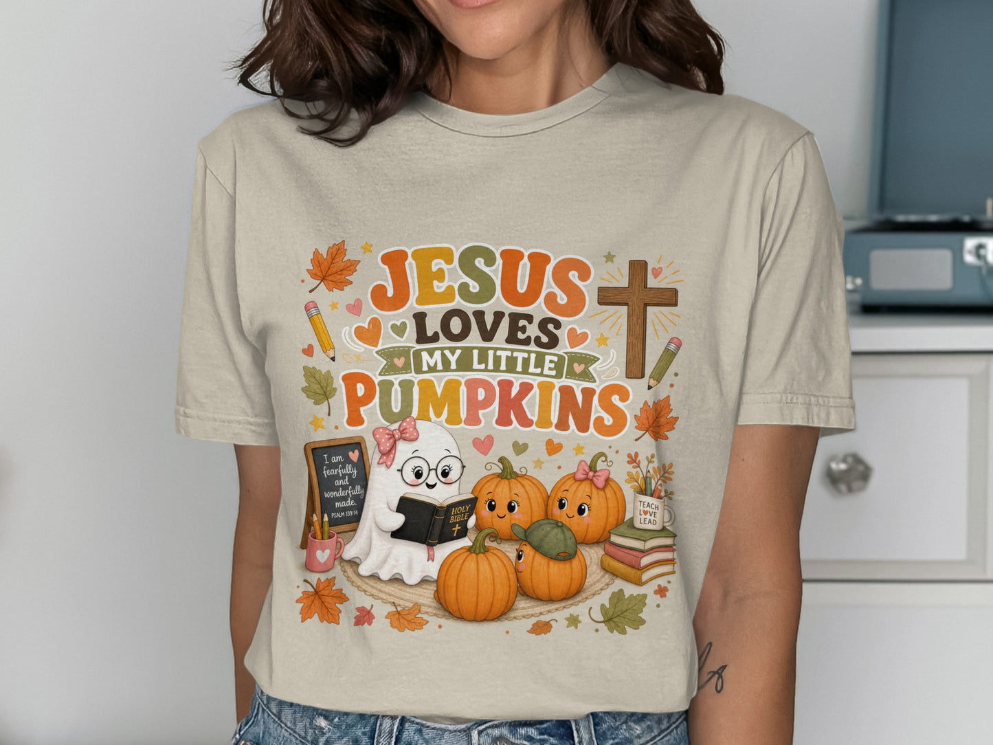T-shirt graphic with text "JESUS LOVES MY LITTLE PUMPKINS", ghost, pumpkins, and Bible.
