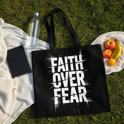 Black tote bag with white text "FAITH OVER FEAR" on grass.
