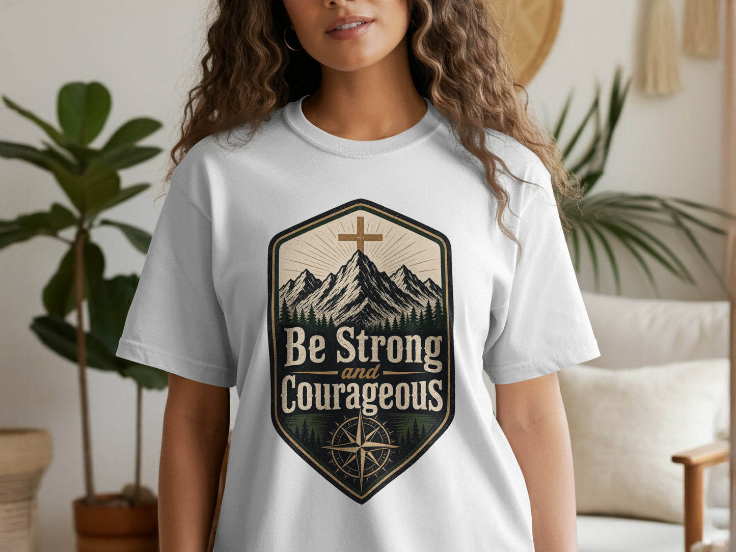 White t-shirt featuring a crest with mountains, a cross, and the text "Be Strong and Courageous".
