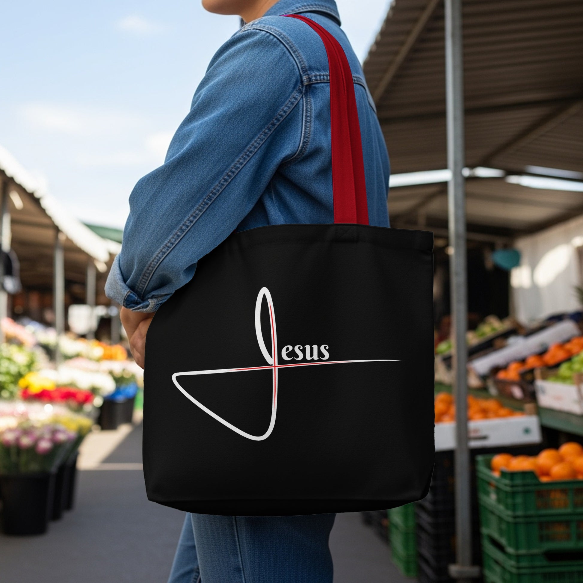 Black tote bag with white "Jesus" text and minimalist red and white cross design.