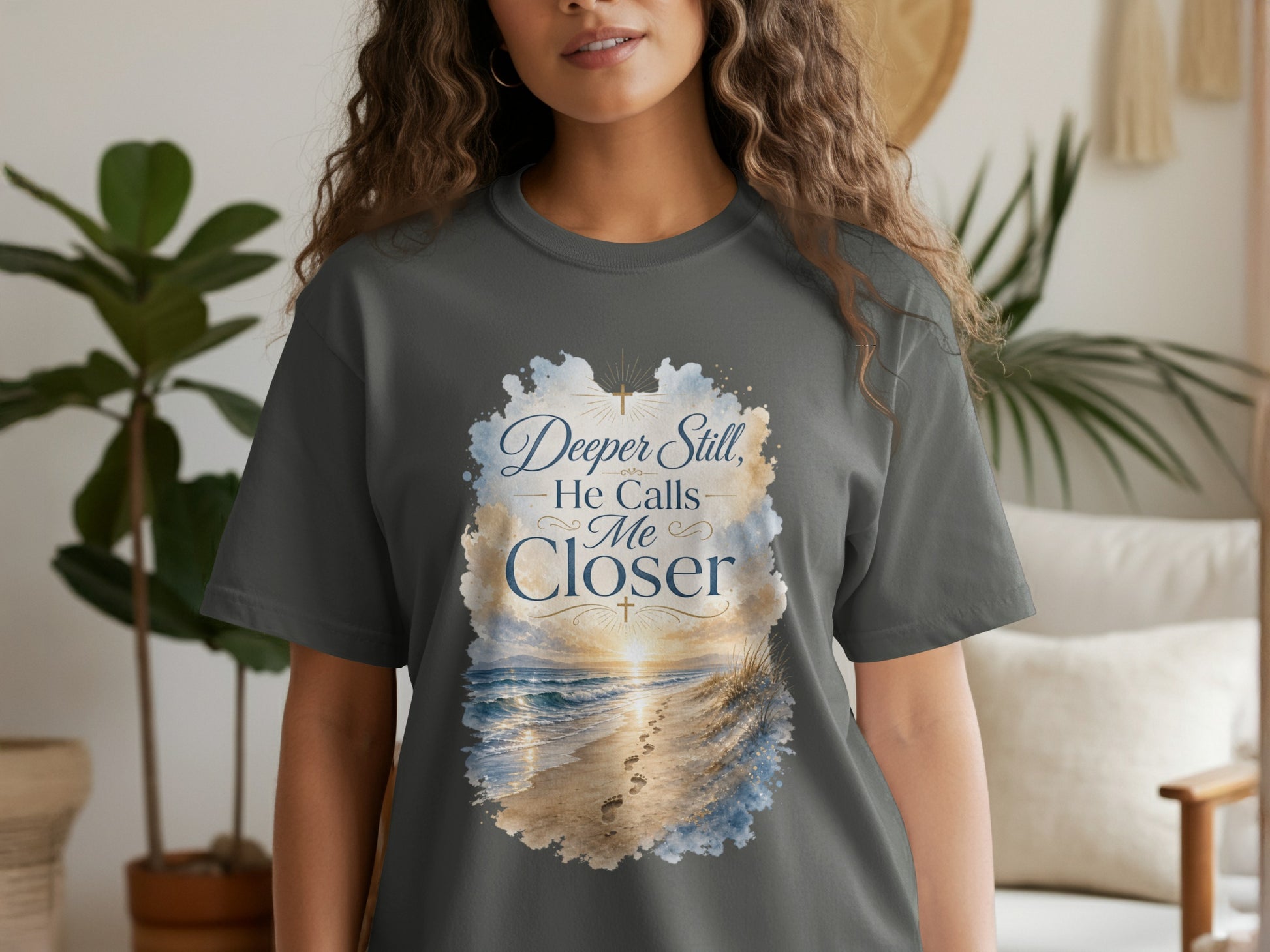 Grey t-shirt with text "Deeper Still, He Calls Me Closer" over a beach scene.