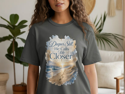 Grey t-shirt with text "Deeper Still, He Calls Me Closer" over a beach scene.