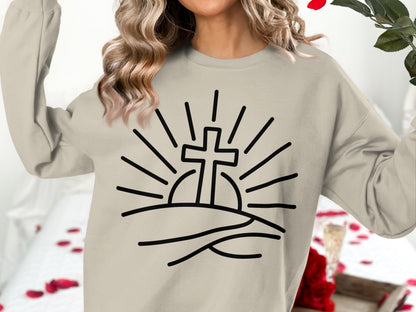Cream sweatshirt with graphic of a cross rising over hills with sun rays.