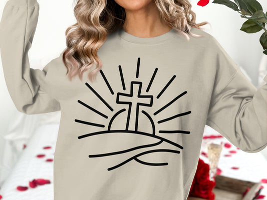 Cream sweatshirt with graphic of a cross rising over hills with sun rays.