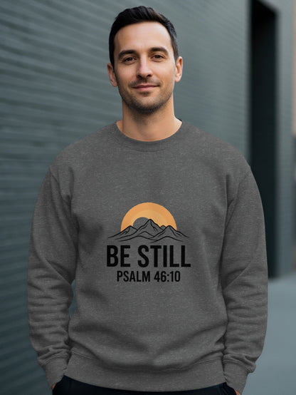 Man wearing gray sweatshirt with mountains, sun, and "BE STILL PSALM 46:10" text.