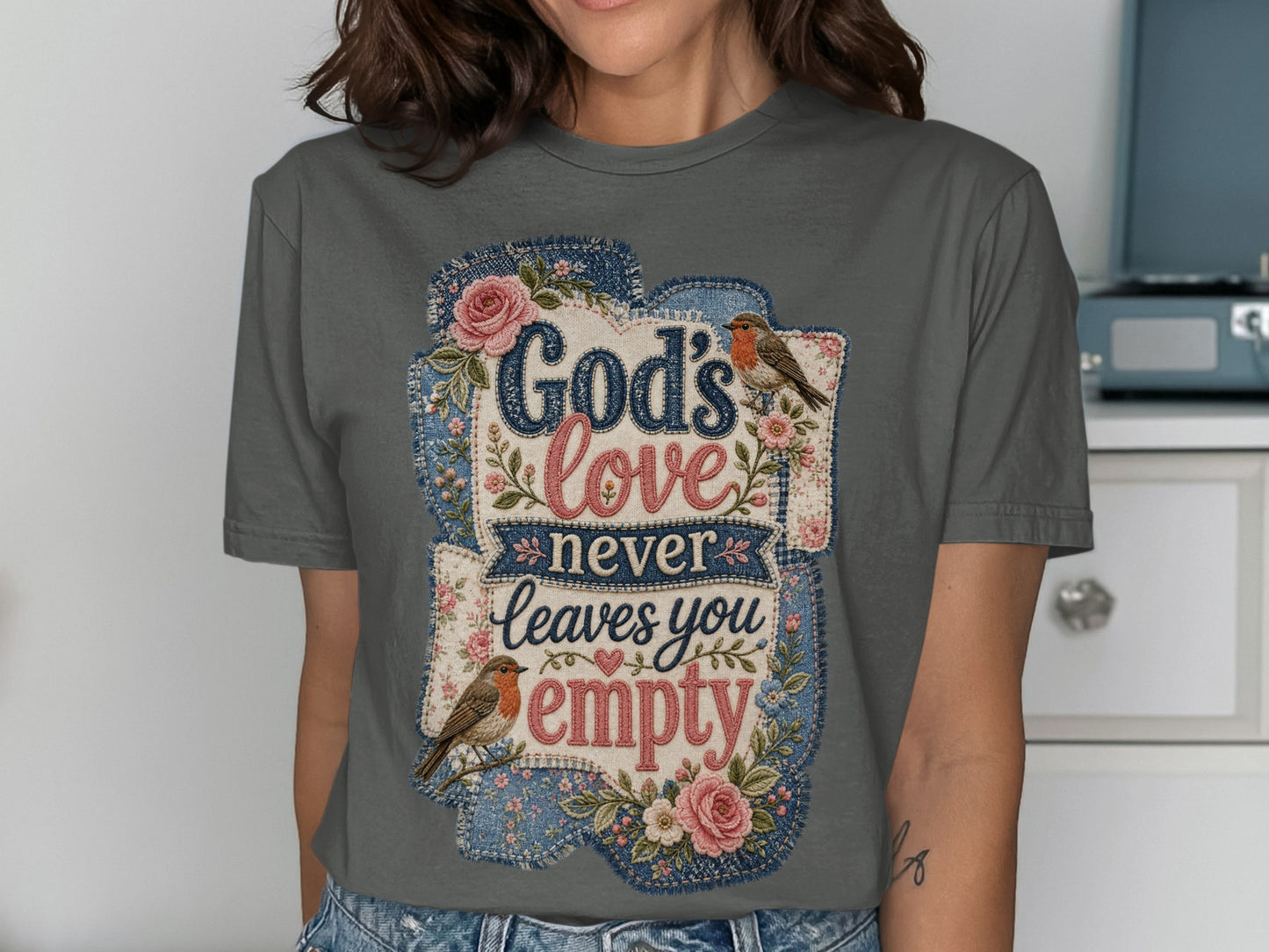 Grey t-shirt with "God's love never leaves you empty" text and floral designs.