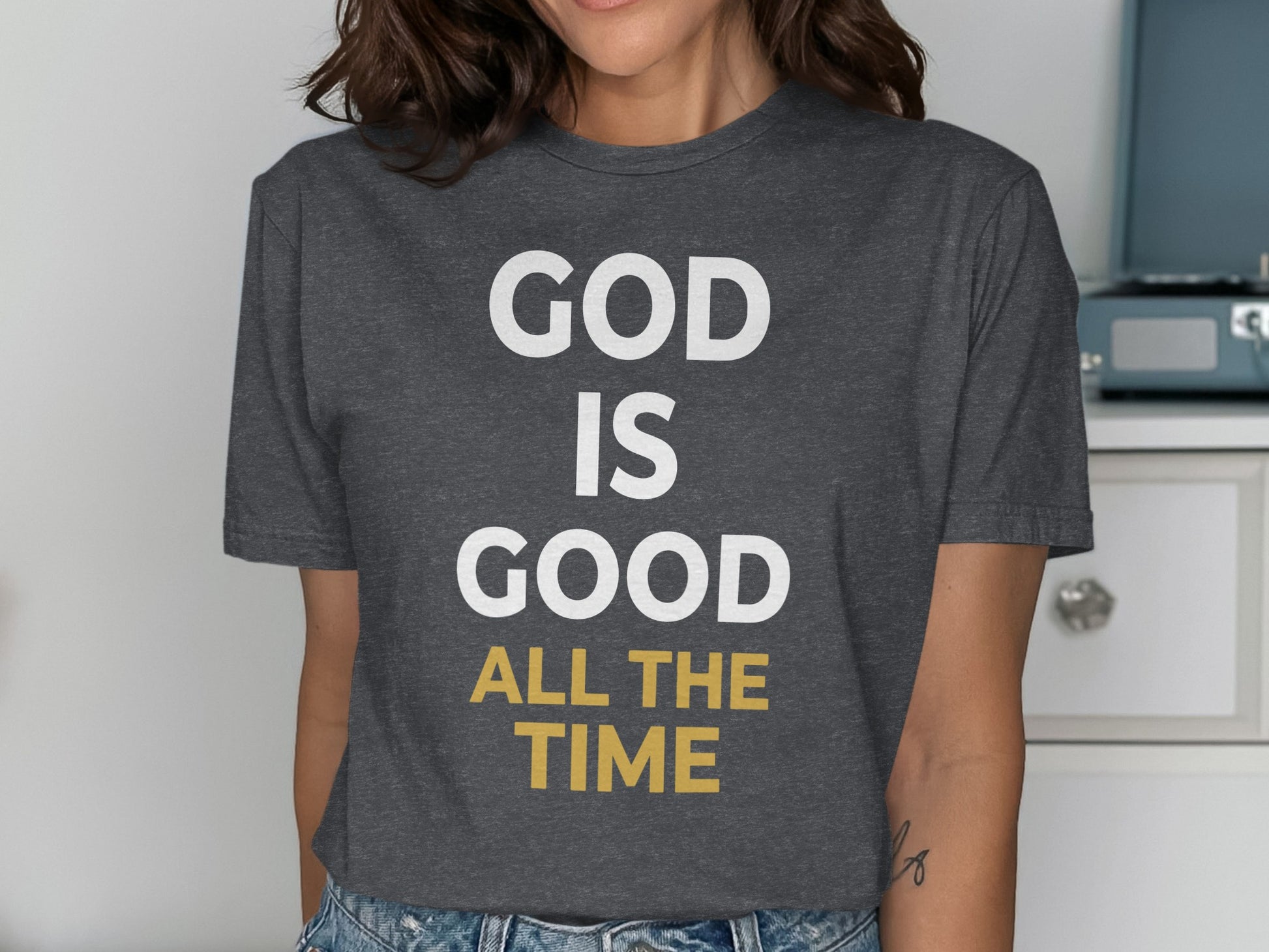 Dark grey t-shirt with white and gold text "GOD IS GOOD ALL THE TIME".