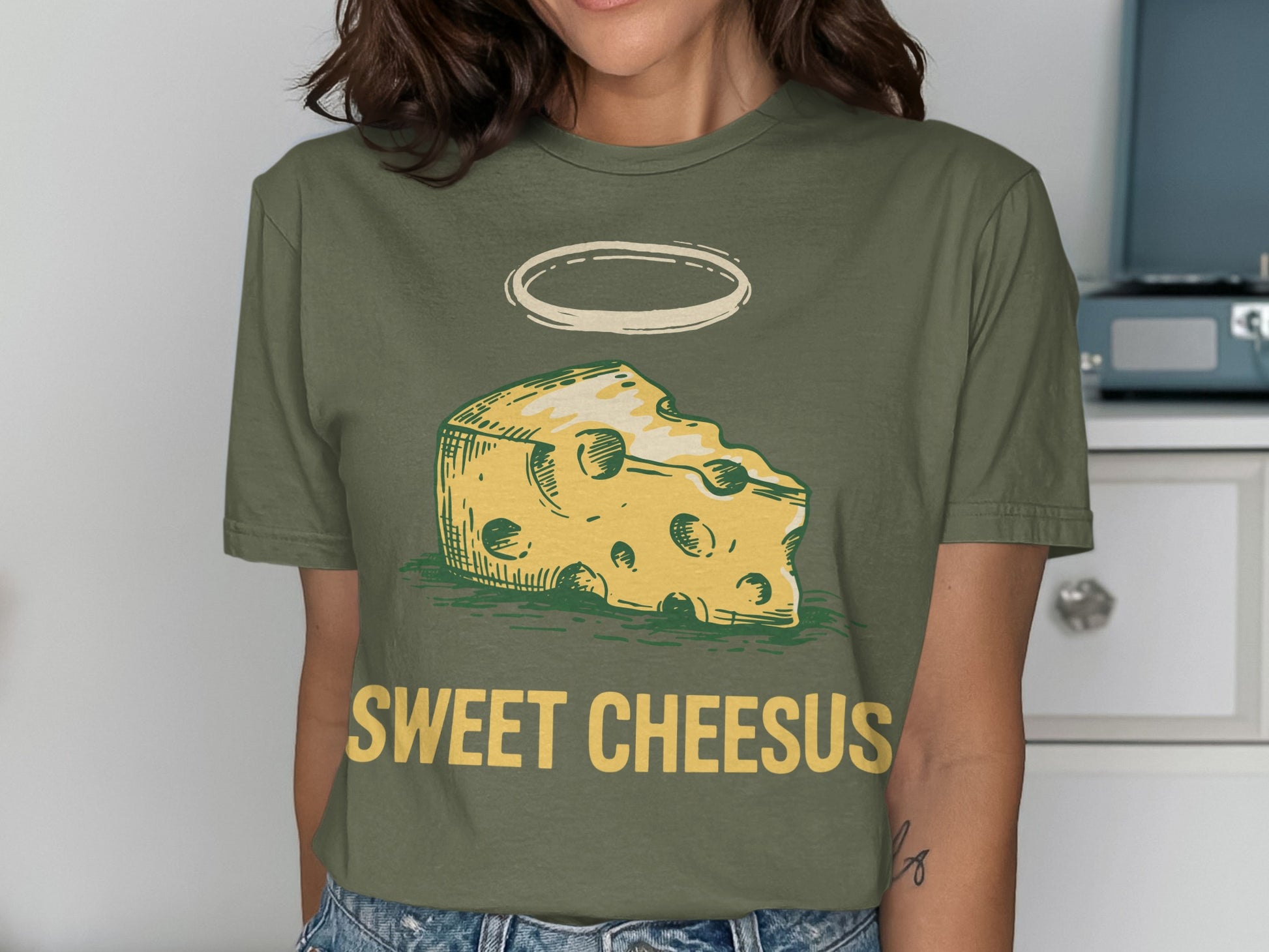 Green t-shirt with a cartoon cheese wedge and halo, text "SWEET CHEESUS".