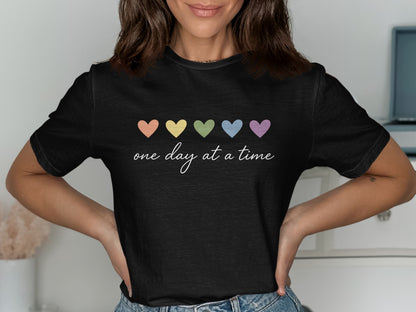 Black t-shirt with pastel hearts and "one day at a time" text.