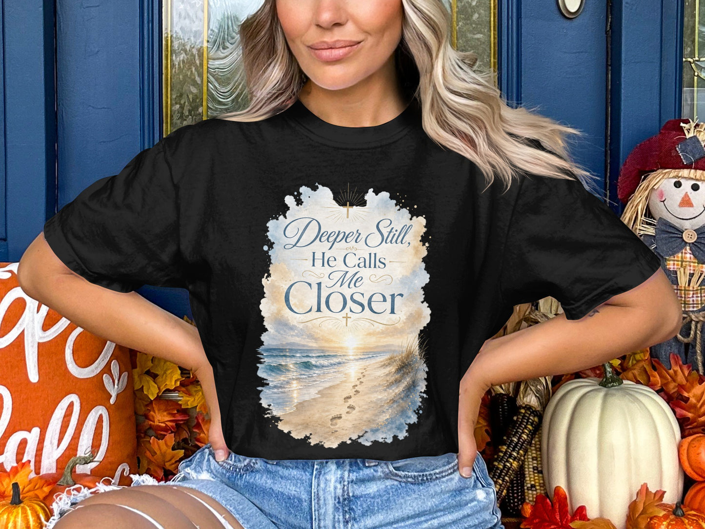 Black t-shirt with "Deeper Still, He Calls Me Closer" text over a beach scene.
