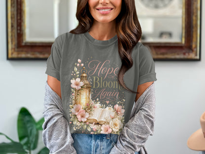 T-shirt with "Hope Blooms Again" text, antique lantern, open book, and floral watercolor art.